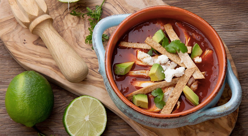 Bowl of sopa de tortilla—the classic Mexican soup—on a table with cutting board and limes